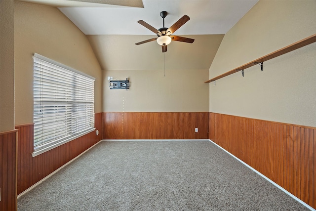 carpeted spare room featuring ceiling fan, wooden walls, and vaulted ceiling