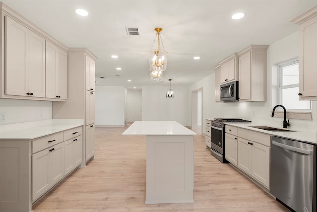 kitchen with sink, stainless steel appliances, pendant lighting, a kitchen island, and light wood-type flooring