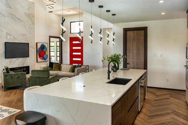 kitchen featuring pendant lighting, parquet flooring, sink, a kitchen island with sink, and a high end fireplace