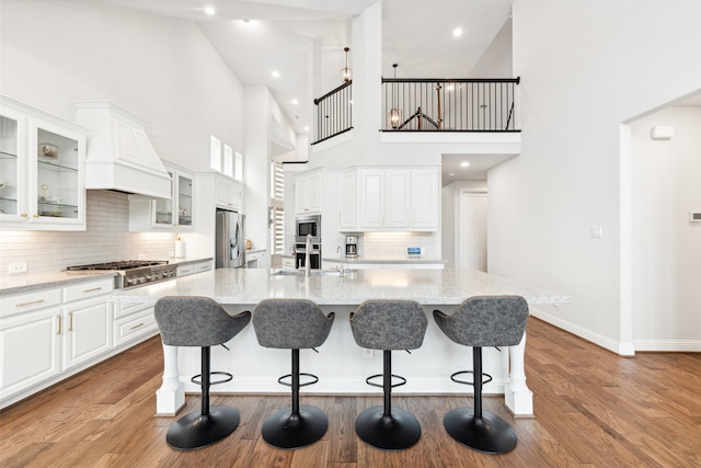 kitchen with appliances with stainless steel finishes, high vaulted ceiling, a kitchen island with sink, and light stone counters