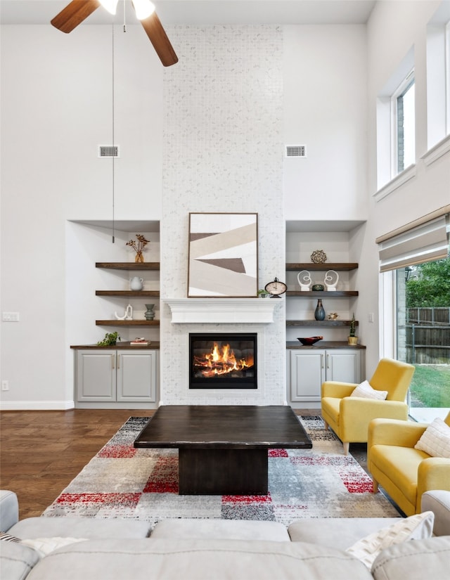 living room featuring a wealth of natural light, a large fireplace, a towering ceiling, and dark wood-type flooring