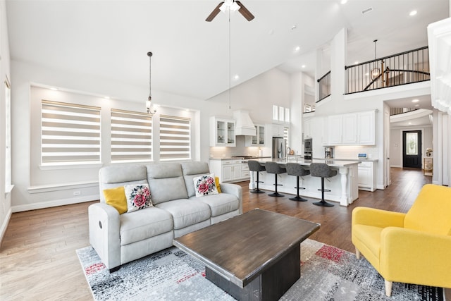 living room with ceiling fan with notable chandelier, light hardwood / wood-style floors, and high vaulted ceiling