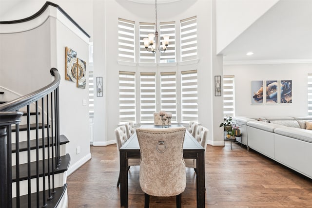 dining area with crown molding, dark wood-type flooring, a towering ceiling, and a chandelier