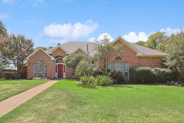 traditional-style home with brick siding, a shingled roof, and a front lawn