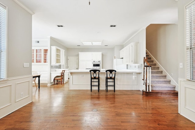 kitchen featuring hardwood / wood-style floors, oven, a kitchen bar, white cabinets, and white refrigerator