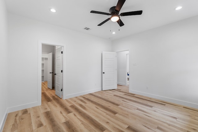 unfurnished bedroom featuring ceiling fan, a walk in closet, and light wood-type flooring