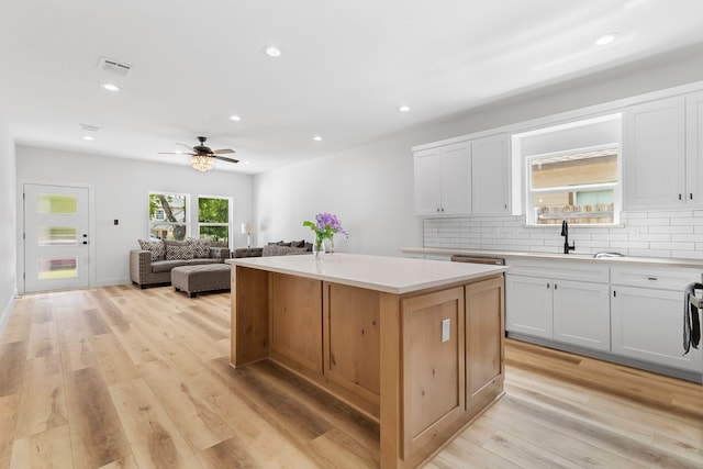 kitchen with ceiling fan, sink, a kitchen island, decorative backsplash, and white cabinets