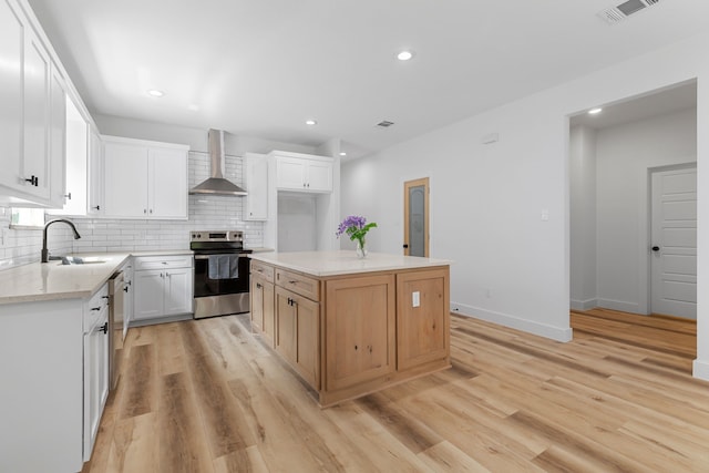 kitchen featuring appliances with stainless steel finishes, a kitchen island, sink, wall chimney range hood, and white cabinetry