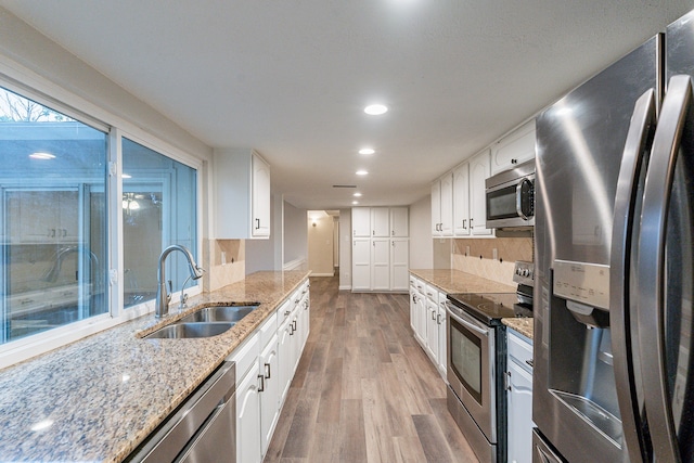 kitchen featuring light stone countertops, stainless steel appliances, sink, hardwood / wood-style floors, and white cabinetry