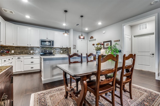 kitchen with black range oven, dark hardwood / wood-style flooring, white cabinets, and hanging light fixtures