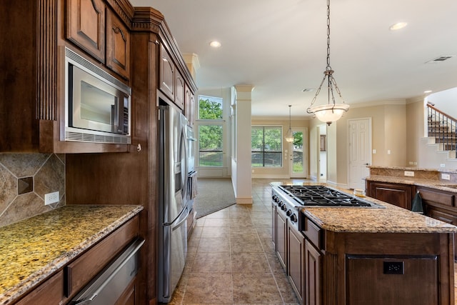 kitchen featuring light stone counters, a kitchen island, decorative light fixtures, and appliances with stainless steel finishes