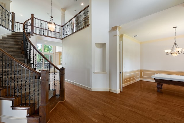 stairway featuring pool table, a high ceiling, hardwood / wood-style floors, a chandelier, and ornamental molding