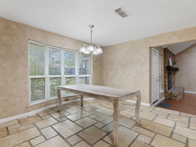 unfurnished dining area featuring a brick fireplace, a chandelier, and a textured ceiling