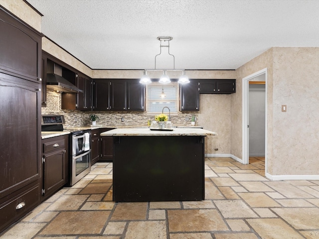 kitchen featuring wall chimney range hood, double oven range, tasteful backsplash, a kitchen island, and decorative light fixtures