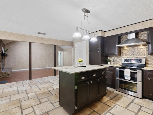 kitchen featuring wall chimney exhaust hood, a center island, pendant lighting, range with two ovens, and backsplash