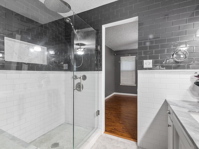 bathroom featuring wood-type flooring, tile walls, vanity, an enclosed shower, and a textured ceiling