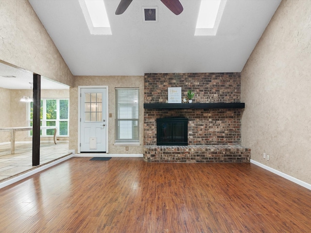 unfurnished living room with hardwood / wood-style flooring, ceiling fan, a skylight, and a brick fireplace