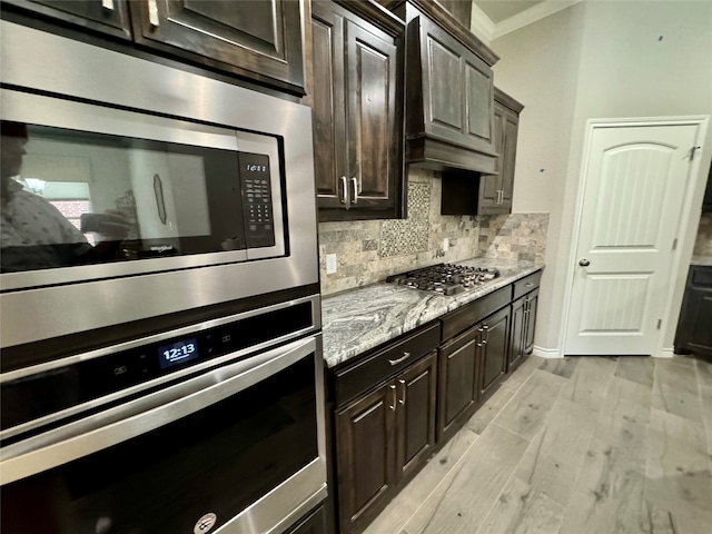 kitchen featuring custom range hood, light hardwood / wood-style flooring, stainless steel appliances, light stone counters, and tasteful backsplash