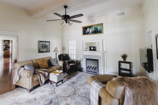 living room featuring beam ceiling, ceiling fan, a high end fireplace, crown molding, and hardwood / wood-style flooring