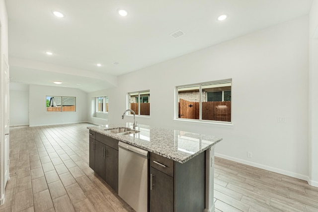 kitchen with dishwasher, sink, light stone countertops, an island with sink, and dark brown cabinets