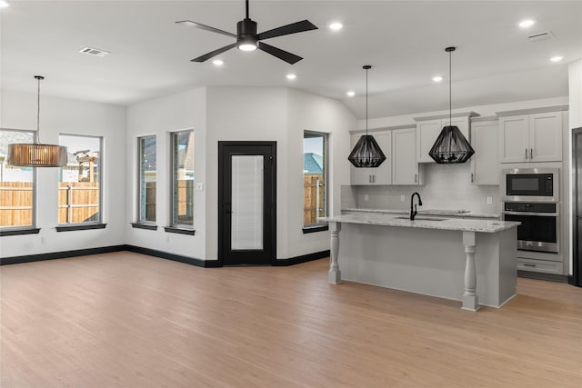 kitchen with light stone countertops, stainless steel appliances, light hardwood / wood-style flooring, a breakfast bar area, and a center island with sink