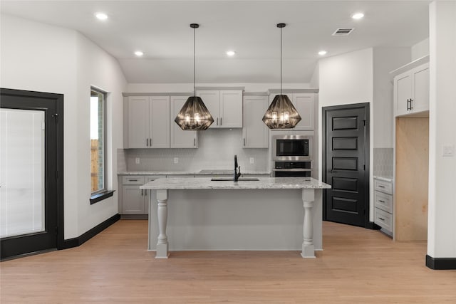 kitchen with pendant lighting, lofted ceiling, a center island with sink, sink, and appliances with stainless steel finishes