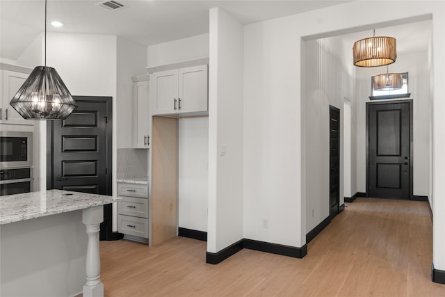 kitchen featuring appliances with stainless steel finishes, decorative light fixtures, white cabinetry, and light stone counters