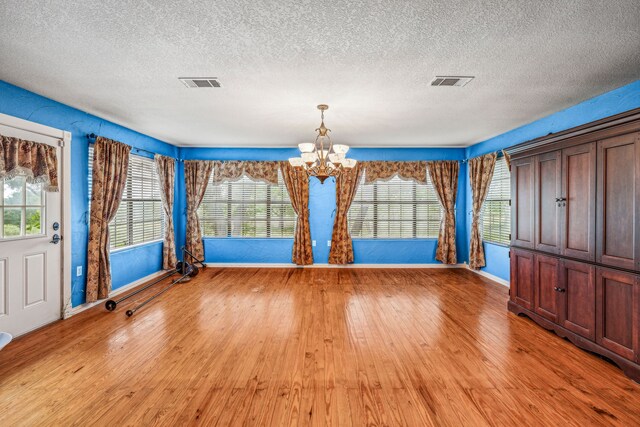 unfurnished dining area with an inviting chandelier, a textured ceiling, and light hardwood / wood-style flooring