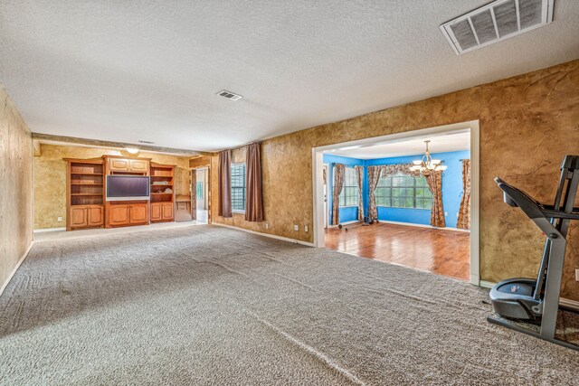 unfurnished living room featuring carpet floors, a textured ceiling, and a notable chandelier