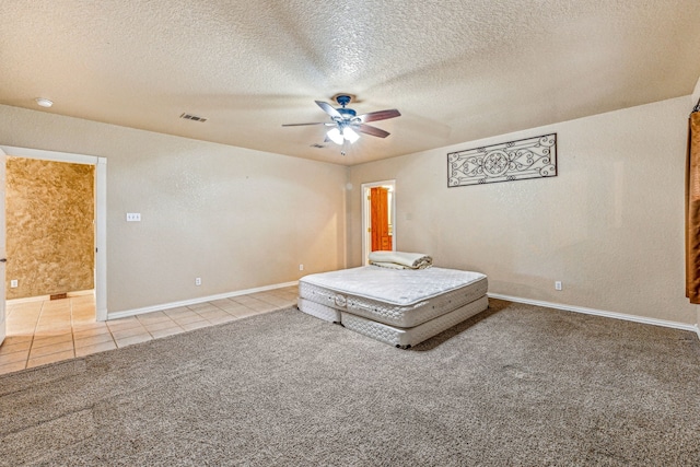 unfurnished bedroom featuring a textured ceiling, tile patterned flooring, carpet flooring, visible vents, and a ceiling fan