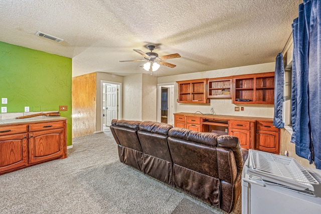 living area featuring a textured wall, wine cooler, light carpet, visible vents, and built in study area