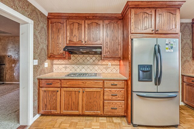 kitchen with tasteful backsplash, light parquet floors, light stone counters, range hood, and appliances with stainless steel finishes