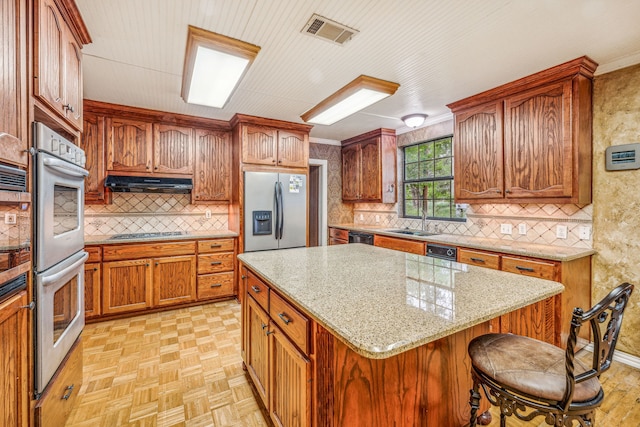 kitchen with light parquet floors, tasteful backsplash, stainless steel appliances, sink, and a center island