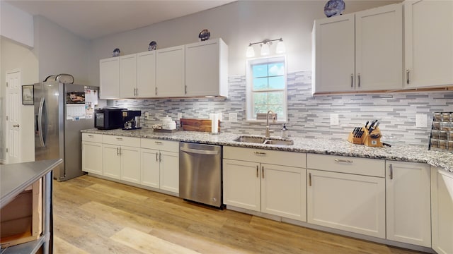 kitchen with light stone countertops, sink, light hardwood / wood-style floors, white cabinets, and appliances with stainless steel finishes