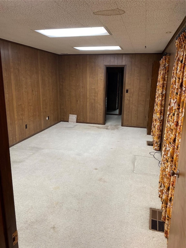 empty room with visible vents, light colored carpet, and wood walls