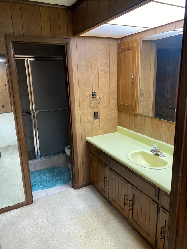 bathroom with a shower with shower door, vanity with extensive cabinet space, wooden walls, and toilet