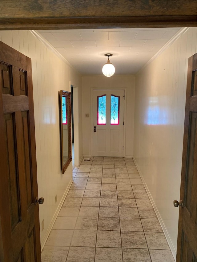 corridor featuring crown molding, light tile patterned floors, baseboards, and wood walls