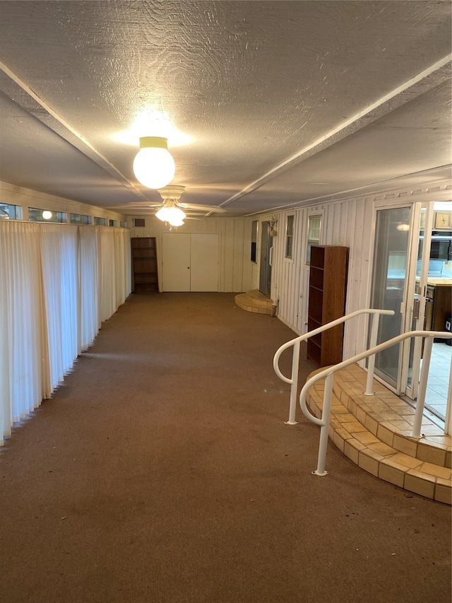 below grade area featuring a textured ceiling, carpet, and a ceiling fan