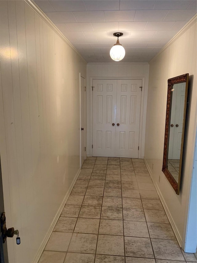 hall with crown molding, light tile patterned flooring, baseboards, and wood walls