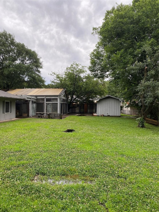 view of yard featuring fence, an outdoor structure, a shed, and a sunroom