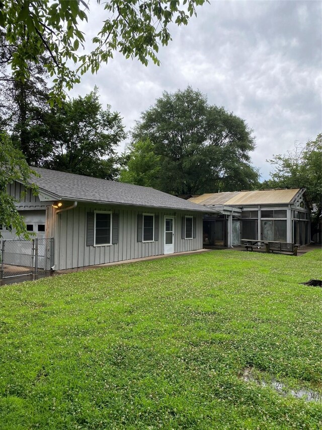 back of property with a yard, a sunroom, board and batten siding, and fence