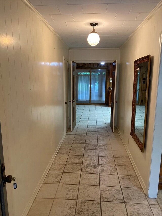hall with light tile patterned floors, baseboards, wood walls, and crown molding
