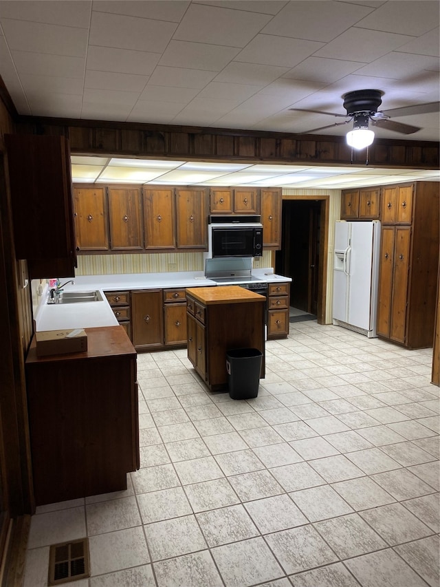 kitchen featuring ceiling fan, white refrigerator with ice dispenser, light tile flooring, a center island, and sink