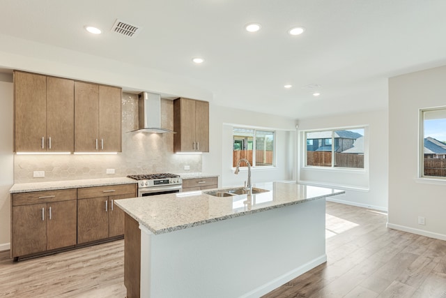 kitchen featuring wall chimney exhaust hood, stainless steel gas range, light hardwood / wood-style flooring, a kitchen island with sink, and sink