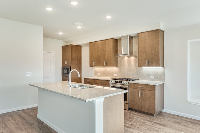 kitchen with light hardwood / wood-style floors, sink, wall chimney exhaust hood, stainless steel appliances, and a center island with sink