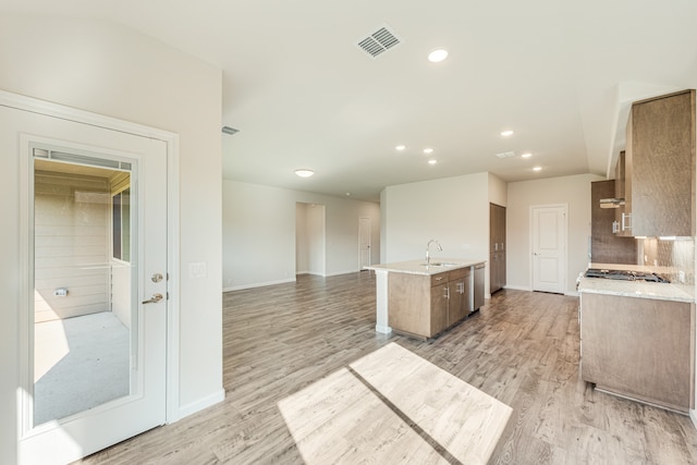 kitchen featuring sink, a kitchen island with sink, wall chimney range hood, dishwasher, and light hardwood / wood-style floors