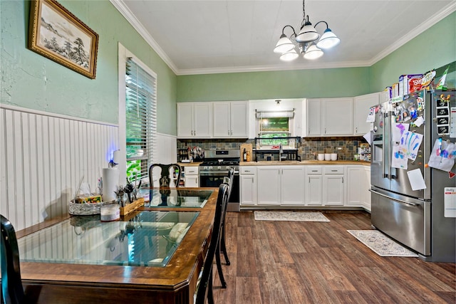 kitchen with crown molding, appliances with stainless steel finishes, hanging light fixtures, tasteful backsplash, and white cabinets