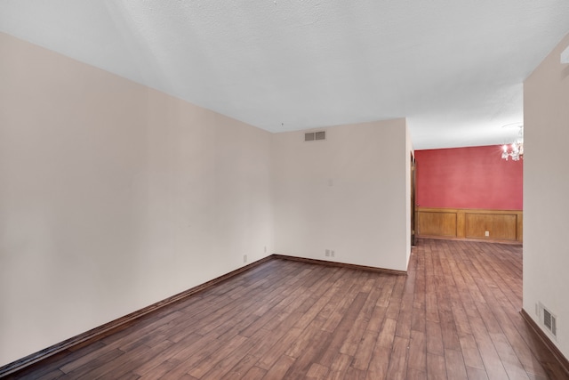 spare room featuring a textured ceiling, hardwood / wood-style flooring, and a notable chandelier