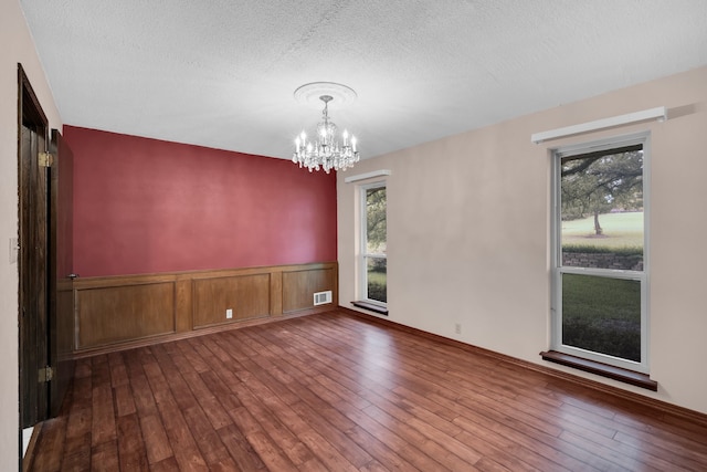 empty room with a chandelier, wood-type flooring, and a textured ceiling