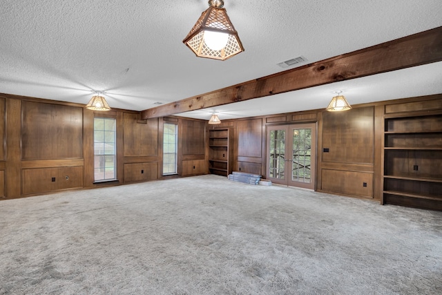 unfurnished living room with carpet flooring, french doors, a textured ceiling, and wooden walls